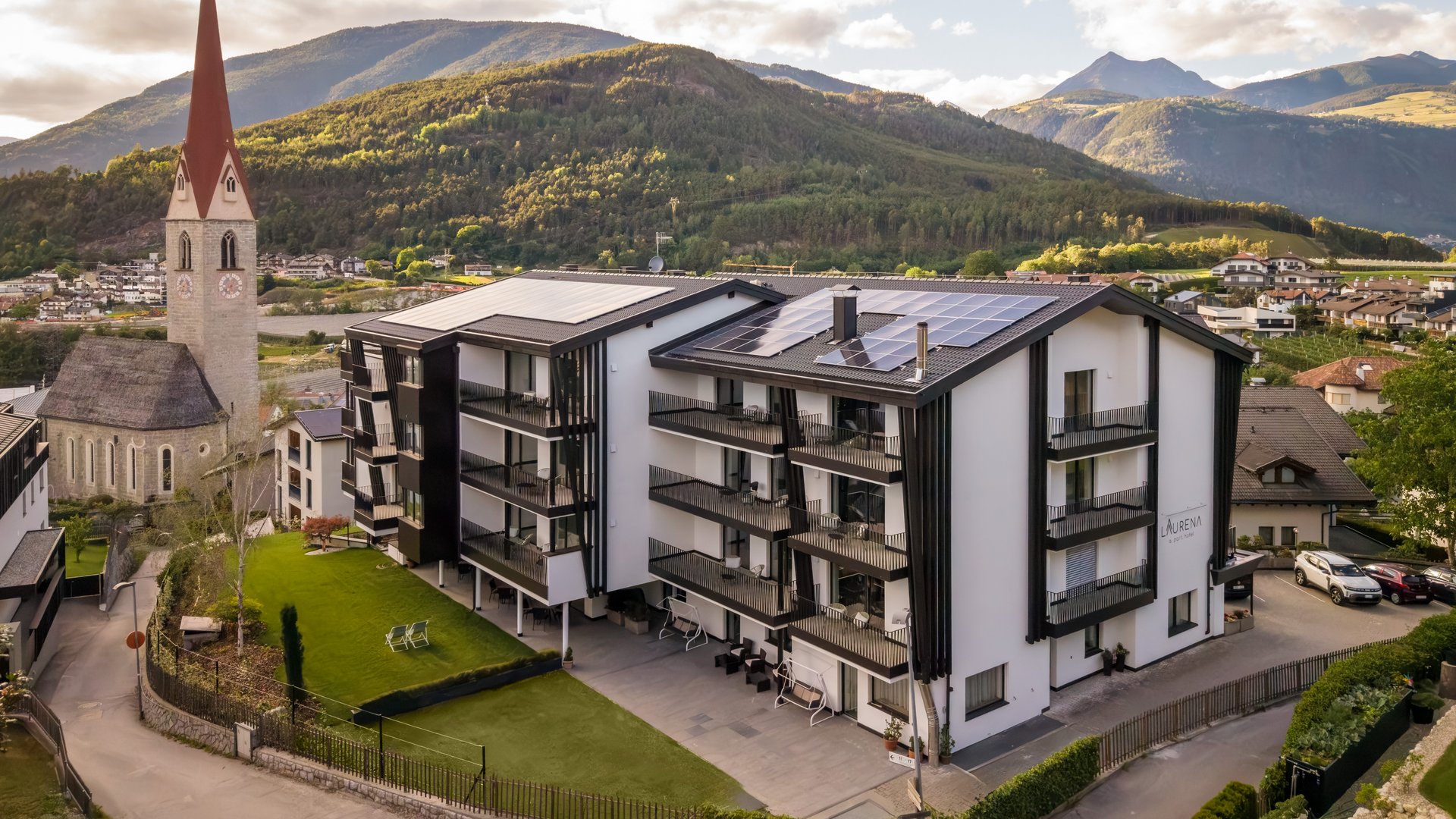 Ihr Hotel in Natz-Schabs bei Brixen, Südtirol Modernes Apartmentgebäude neben Kirche vor bewaldeten Bergen